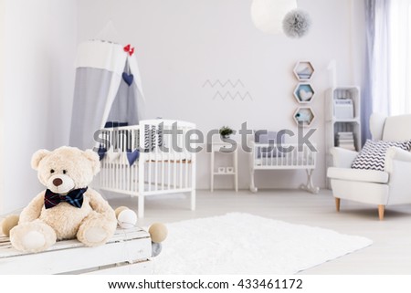 Light and spacious baby room with white furniture, teddy bear in the foreground