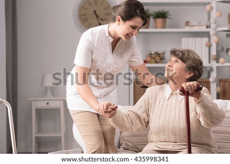 Young carer supporting senior disabled woman with walking stick.