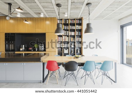 Interior in an industrial style with an open kitchen, dining table and colorful chairs