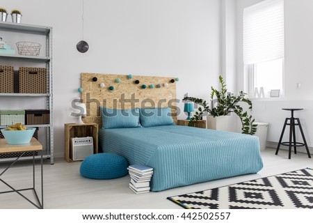 Spacious bedroom with large bed, blue bedding and simple, new furniture, white walls