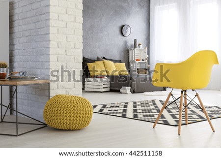 Spacious bedroom with white brick wall. Wooden coffee table and yellows chairs. By the wall grey bed with yellow pillows