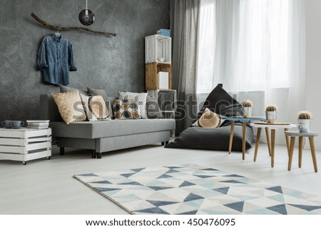 New apartment interior in grey with sofa, modern pouf, small table, two chairs and pattern carpet