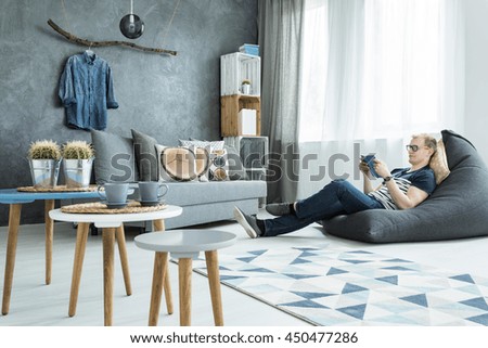 Modern style interior in grey with sofa, stylish futniture, man sitting on a bean bag