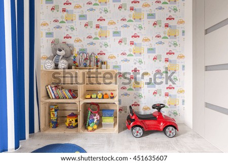 Small room with colorful wallpaper designed for boy. By the all wooden shelves with toys and little car