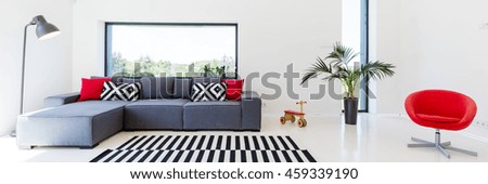 White interior of a living room with a couch with cushions, lamp, red minimalistic armchair and striped carpet