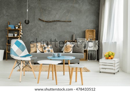 Modern minimalistic and bright living room in shades of cyan with sofa, chair, three coffee tables, carpet and stillage made of wooden cases