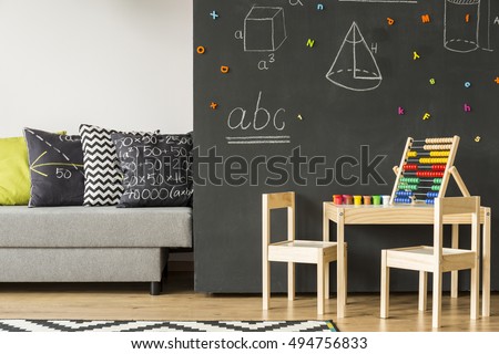 Sofa standing next to a chalkboard wall with geometrical figures, in the foreground small table and wooden chairs
