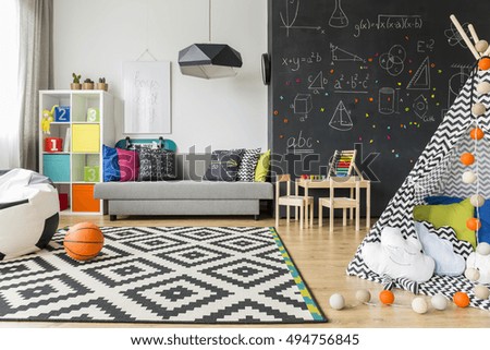 Spacious black and white child room with window, sack chair, regale, sofa, carpet, chalkboard wall, small table, chairs and play tent