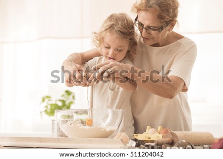 Senior nanny helping child to break the egg into a bowl