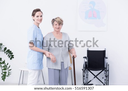 Smiled elder woman with cane, supported by her female nurse