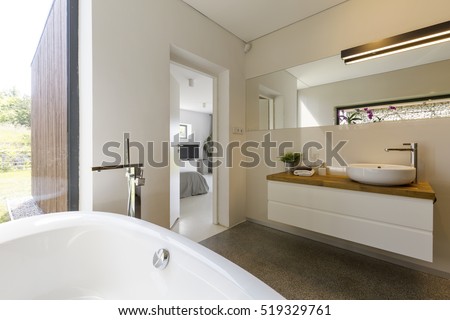 Modern spacious bathroom with white bathtube with garden view throught panoramic window