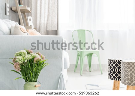 Light room with upholstered stools, sofa, green chair and flowers