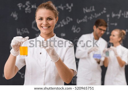 Happy scientist holding a laboratory glassware with orange liquid