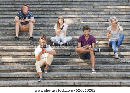 People sitting on city stairs, using their phones
