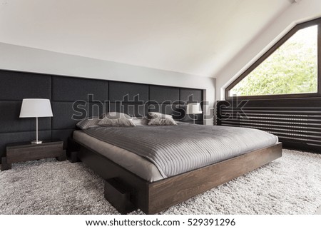 Elegant large bed in a dark frame in an attic bedroom