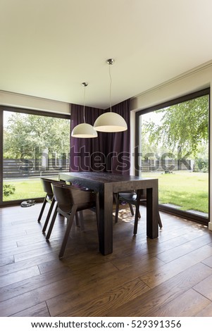 Dark table and chairs in a dining room with large windows overlooking the garden
