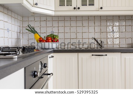 Cropped picture of a kitchen with white furniture and a bowl of vegetables