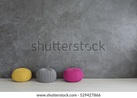 Three colorful wool poufs in concrete wall interior