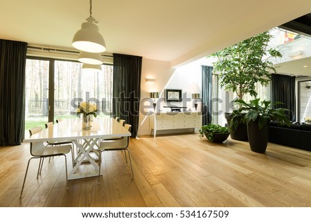 Open spacious room with large windows, minimalist dining table with chairs, plants and pendant lamps