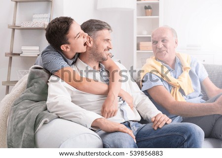 Son embracing his father, grandfather sitting on sofa and smiling