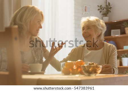 Woman sitting beside table while talking with her old mother