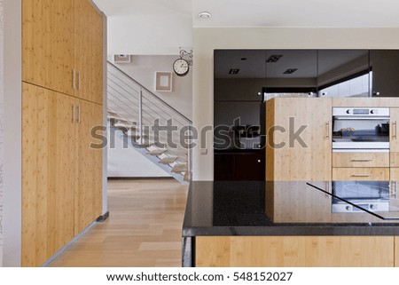 Spacious kitchen with wooden furnitures, kitchen island with marble countertop and stais in the back