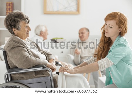 Young caregiver taking care of older disabled woman in nursing home