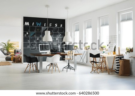 Modern workspace with blackboard calendar, desk, chairs and computers