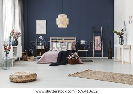 Painting hanging on dark blue wall in cozy bedroom with fresh flowers