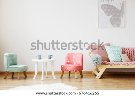 White table with tea cups and chairs for children in baby room with poster on the wall