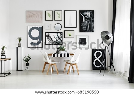 Dining table by the white wall with posters in spacious lounge