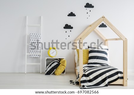 Stylish, modern child's bedroom with a large, yellow alarm clock, black rainy cloud stickers on the wall, and a wooden bed with striped bedding