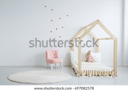 Modern children\'s furniture in a spacious bedroom with star stickers on the white wall, and a pastel pink comfortable chic chair next to a wooden bed