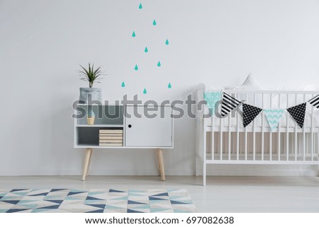 Cozy interior of kid\'s bedroom with a mint water drop stickers on the wall, a plant standing on a cupboard, and a small bed for a baby decorated with washi tape