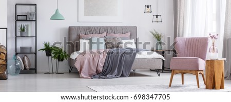 Powder pink chair standing in a bedroom next to a wooden stool and a flower on it