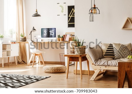 Modern loft interior full of natural wooden furniture and accessories with desk, computer, white chest, beige sofa, table and paper pots for plants