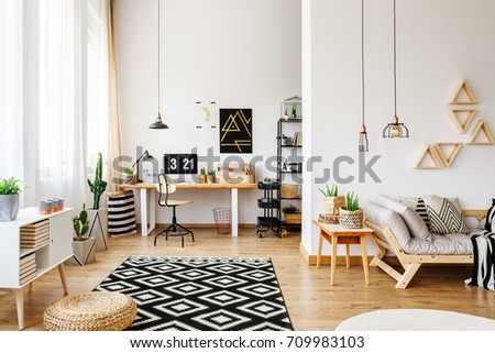 Modern white craft room in open apartment with creative design, triangle shelves, industrial pendant lamps, wooden furniture, patterned rug, hardwood floor, sofa and desk