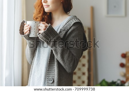 Young woman with mug standing next to a window