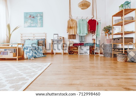 Blue painting above king-size bed with blue coverlet in bedroom with boho wardrobe in modern interior