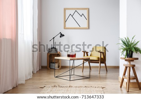 Rustic design of white apartment interior with designer armchair, modern coffee table and framed poster on the wall