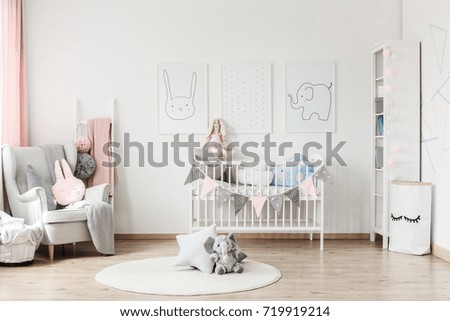Plush toy and pillow on white round carpet in baby\'s room with grey armchair and posters on wall