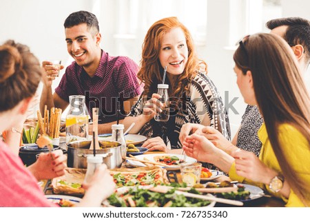 Group of mixed-race people celebrating vegan party at home, sitting at colorful table full of healthy snacks, salads and organic dishes
