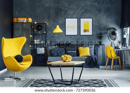 Table on black and white carpet in hygge style living room with designer yellow chair