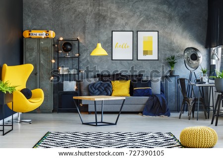 Yellow lamp above table in living room with grey sofa, yellow pouf and designer chair