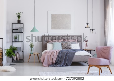 Retro pink chair in adorable pink bedroom with pastel bedding on bed and flowers in glass color vase on table