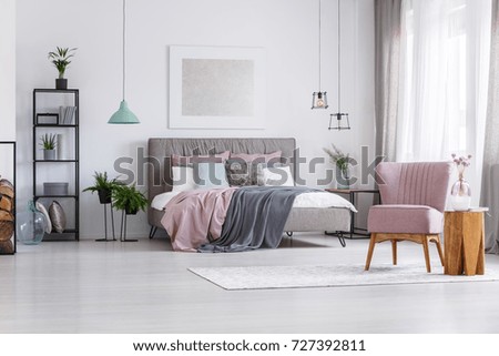Flowers in glass vase on wooden table next to pink chair in woman bedroom with pastel accents