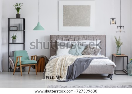 Silver painting above king-size bed with knit beige blanket in adorable bedroom with mint retro chair