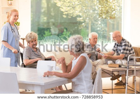 Group of seniors spending free time in bright living room with big window at nursing house