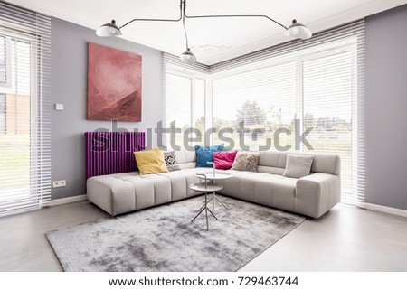 Two small tables standing on a soft, grey carpet by the sofa in the corner of a living room and an abstract painting on the wall