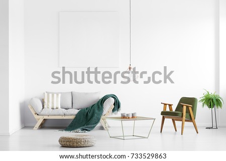 Dark green blanket thrown on grey sofa in bright living room with empty poster and armchair